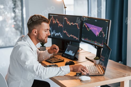 Preview: Using laptop. Young businessman in formal clothes is in office with multiple screens