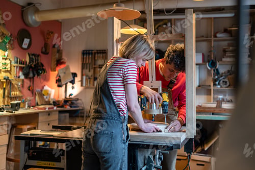 Preview: Carpenters married couple in workplace, teamwork. Careful attentive wife helps husband in work.