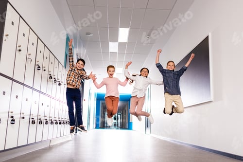 Preview: Four smiling pupils jumping in corridor during brake in school