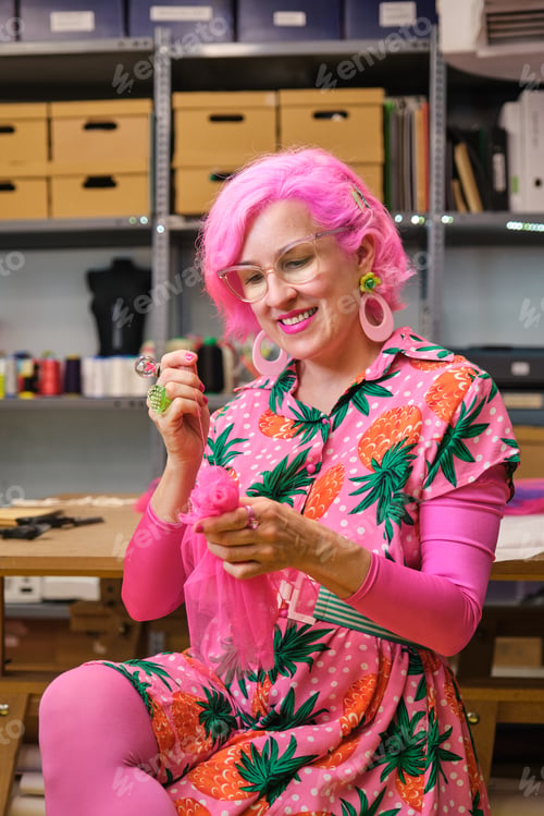 Preview: Dressmaker with pink hair and colorfull clothes hand sewing a piece of fabric.