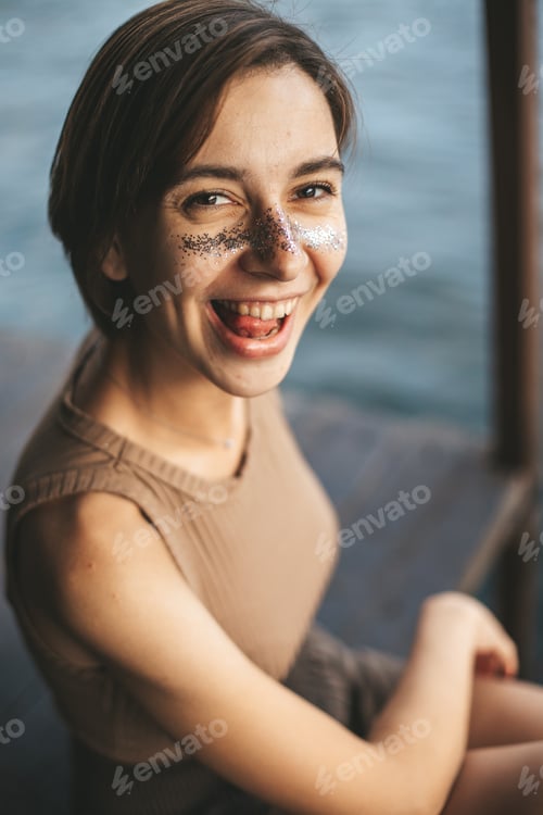 Preview: Young woman with glitter on face sitting on lake house