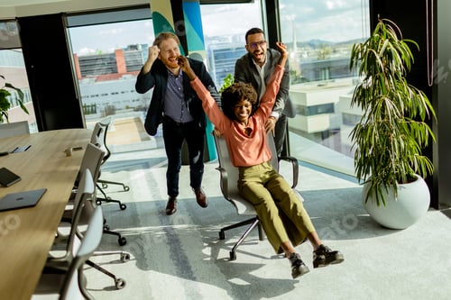 Preview: Jubilant Office Celebration Captures Colleagues Spontaneous Chair Race in Sunlit Room