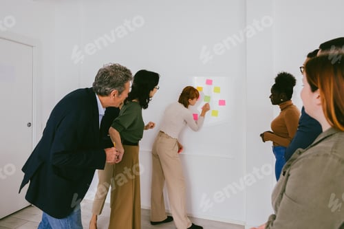 Preview: Multi-ethnic business people meeting at office using post it notes to share ideas on white wall