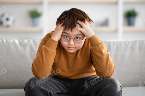 Preview: Stressed chinese boy looking at camera, home interior