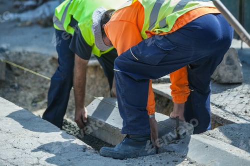 Preview: Workers with special uniforms installing a sidewalk in a hole filled with concrete