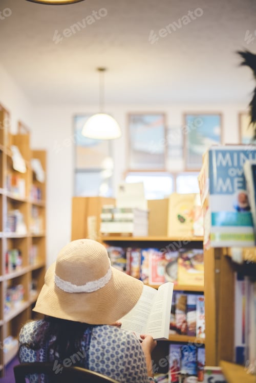 Preview: Vertical shot of a female wearing a summer hat and reading a book in the library