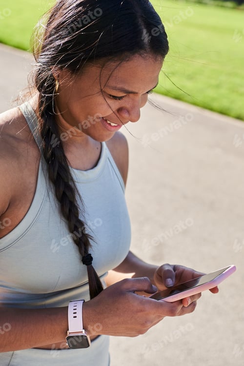 Preview: African millennial woman using smartphone in park after training