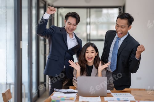 Preview: Asian business team celebrating success with raised fists at office