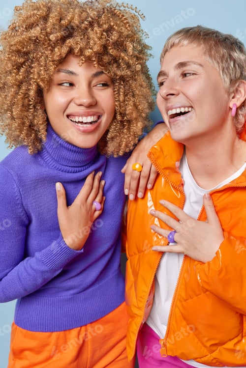 Preview: Overjoyed young women laugh and look happily at each other have fun keep hands on chest feel very