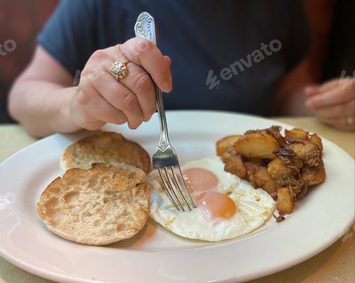 Preview: Eating breakfast. Unrecognizable middle aged baby boomer woman eats eggs.