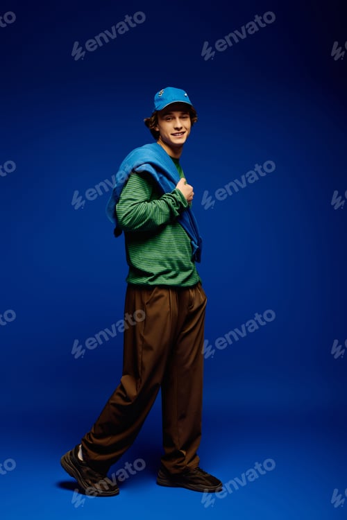 Preview: Young man showcases modern fashion with stylish confidence in vibrant blue background