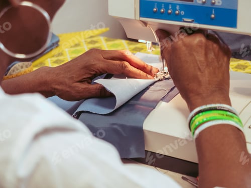Preview: close up of adult black seamstress desginer hands use sewing machine to sew a shirt with precision