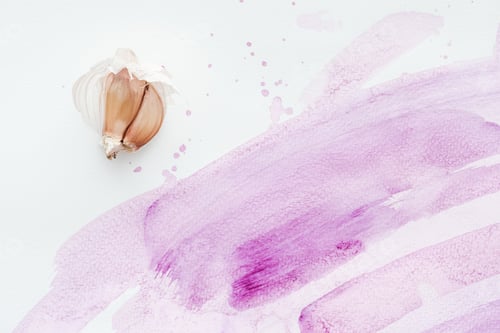 Preview: top view of raw garlic on white surface with pink watercolor strokes and blots