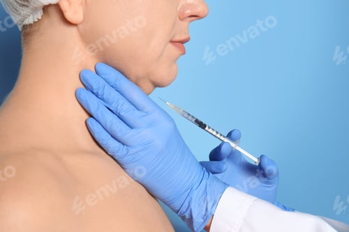 Preview: Mature woman with double chin receiving injection on blue background, closeup
