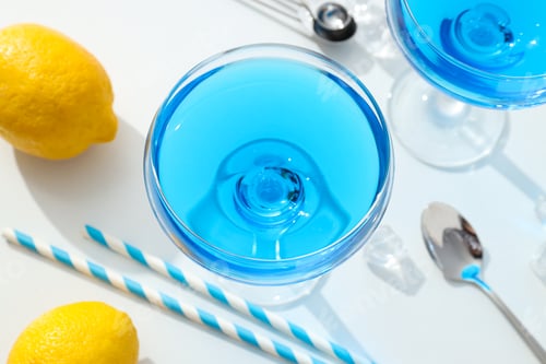 Preview: Blue cocktail in glass, whole lemon, straws and ice cubes on white background, top view