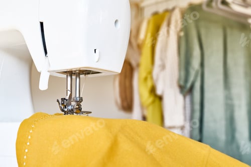 Preview: Close up of sewing machine with yellow linen fabric and linen clothes in background.