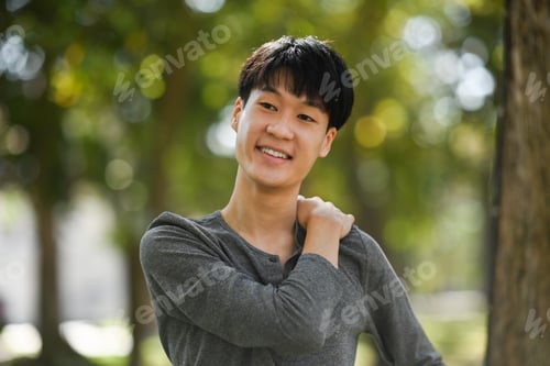 Preview: Pleasant asian man in casual clothes relaxing, stretching arms while standing in the park outdoors.