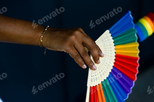 Preview: Human hands hold LGBTQ pride fan and wristband