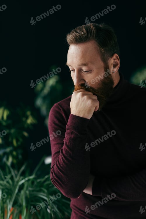 Preview: Pensive bearded man in jumper looking away near blurred plants isolated on black