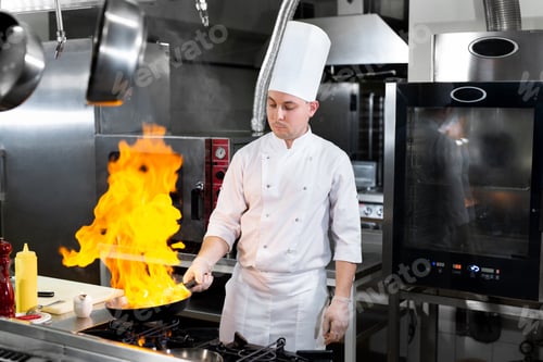 Preview: Chef cooking with flame in a frying pan on a kitchen stove.