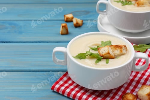 Preview: Bowls with tasty creamy soup of parsnip on light blue wooden table, space for text