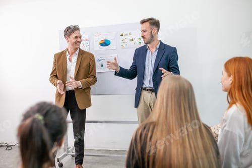 Preview: business team male and female colleagues talking at work share ideas with chart on board.