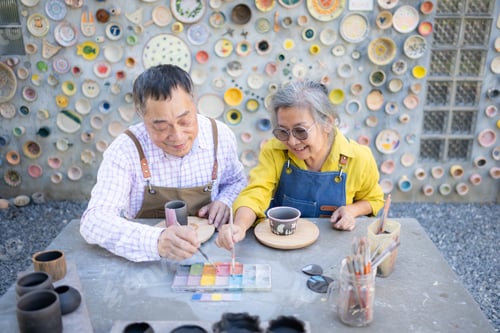 Preview: Asian retired couple is engaged in pottery making and clay painting activities.