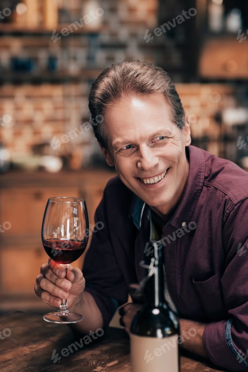 Preview: handsome smiling man holding glass of wine and looking away