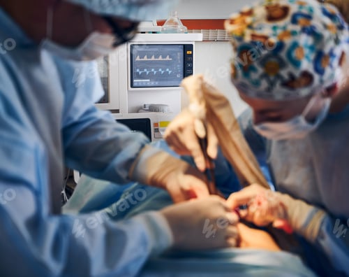 Preview: Doctors doing plastic surgery in operating room with patient monitor.