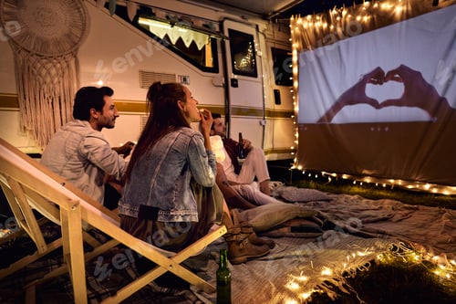 Preview: Group of young cheerful people watching a movie on camping site