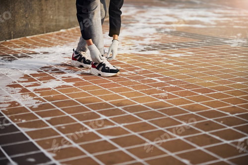 Preview: Person lacing her shoes standing on a pavement