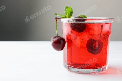 Preview: Tasty cherry soda with ice cubes, mint and berries on white wooden table, closeup. Space for text