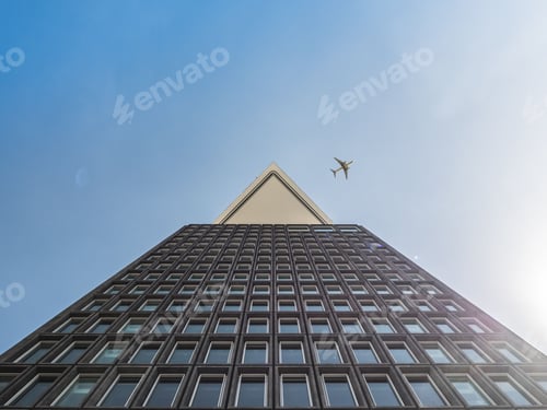 Preview: Low angle shot of modern high-rise building with an airplane soaring in the background