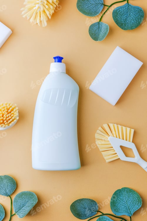 Preview: Clean bottle with brushes and sponges on peach backdrop with green leaves.