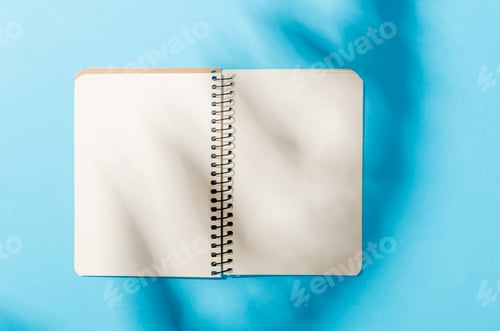 Preview: Blank notebook mockup with shadow of leaves on blue background.