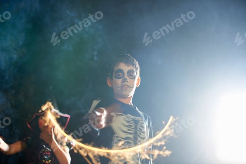 Preview: Brother and sister wearing halloween costumes playing with sparklers in garden at night