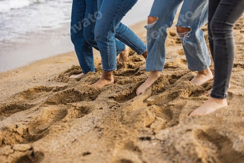 Preview: Friends wearing jeans are enjoying walking barefoot on the beach
