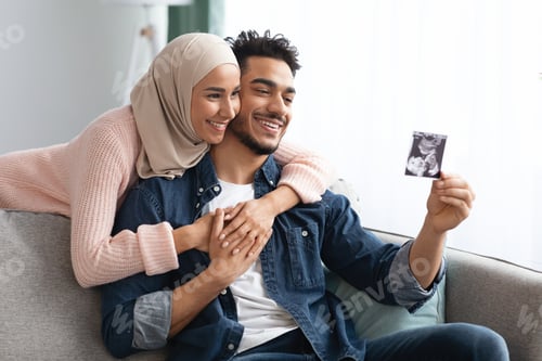 Preview: Pregnant Muslim Woman And Husband Looking At Baby Sonogram Picture At Home