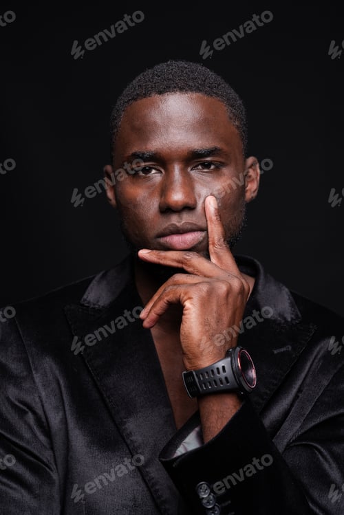 Preview: Pensive African American businessman with hand on chin looking at camera on black background