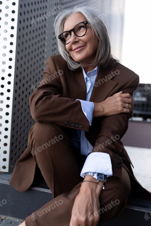 Preview: charming gray-haired well-groomed middle-aged woman in glasses dressed in a brown jacket on the