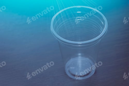 Preview: Transparent plastic cup on the table. View from the front from above. Rays of blue color.
