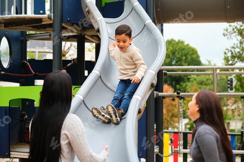 Preview: Lesbian couple playing with their son in the slide at children's playground.