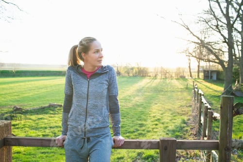 Vista previa: Woman wearing sports clothing leaning against fence looking away