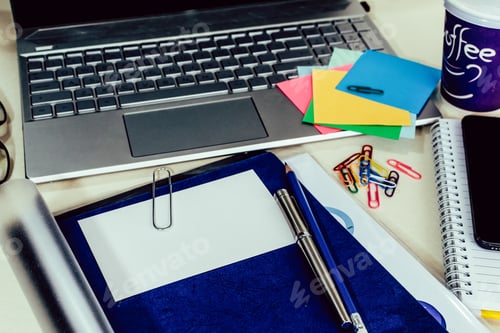 Preview: Top view closeup of a laptop, notebook, smartphone, paper clips and a cup of coffee on the desk