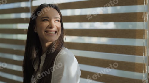 Preview: Smiling happy inspired Caucasian playful businesswoman catch sunbeams looking at sun light in window