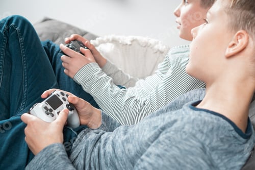 Preview: School aged boys sit on sofa with game joysticks, side view from above. Children play videogames