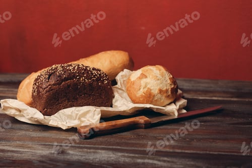 Preview: loaf of rye bread and flour products on paper packaging knife on a wooden table and red background
