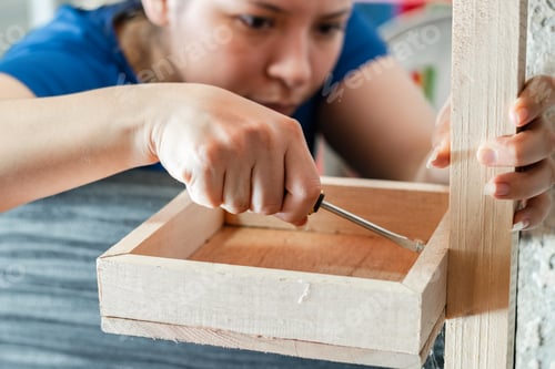 Preview: young woman using a screwdriver to tighten a screw on a wooden shelf