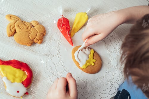 Preview: Close-up of children's hands coloring egg-shaped cookies with icing.
