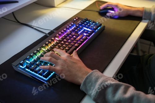 Preview: Caucasian man using the keyboard of his gamer computer with LED lights and playing games